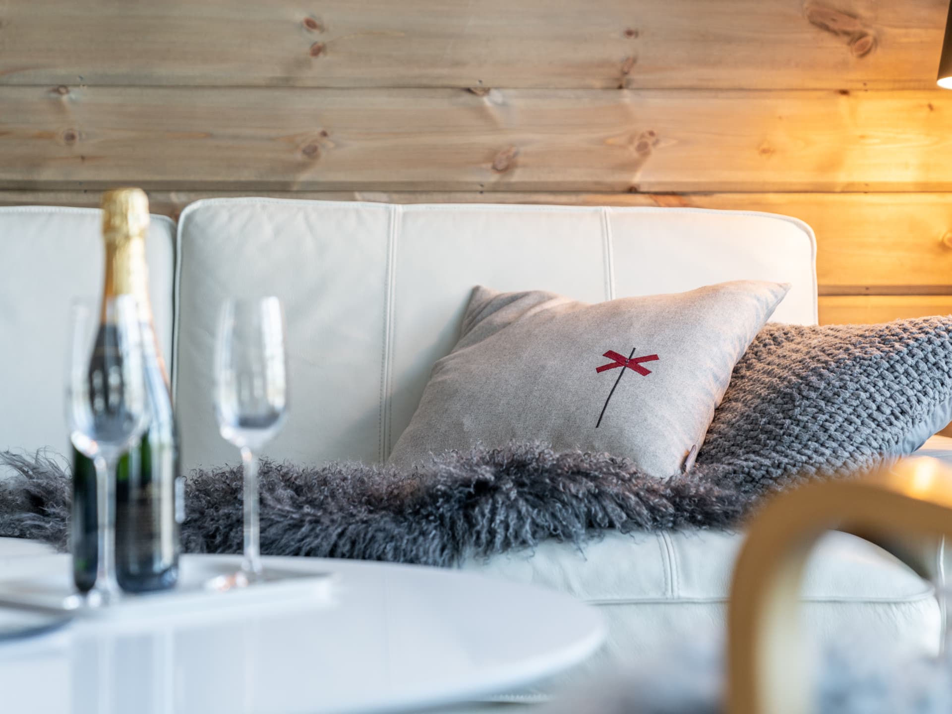 Detalj med kudde med rött ledkryss, fårskinn och champagne på soffbordet